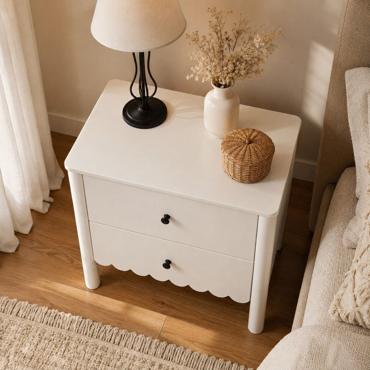 White nightstand with a lamp, vase, and basket in a bedroom setting.