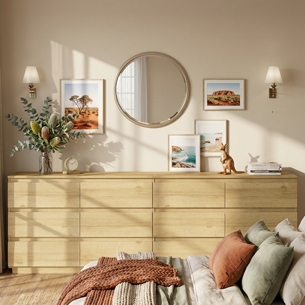 Neatly made bed with decorative pillows and a wooden dresser in a bedroom setting.