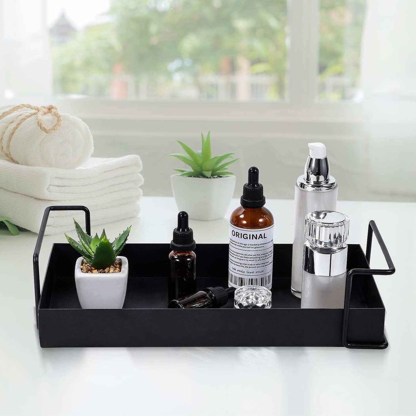 Black metal bathroom vanity tray with essential oils and decor items on a white countertop.