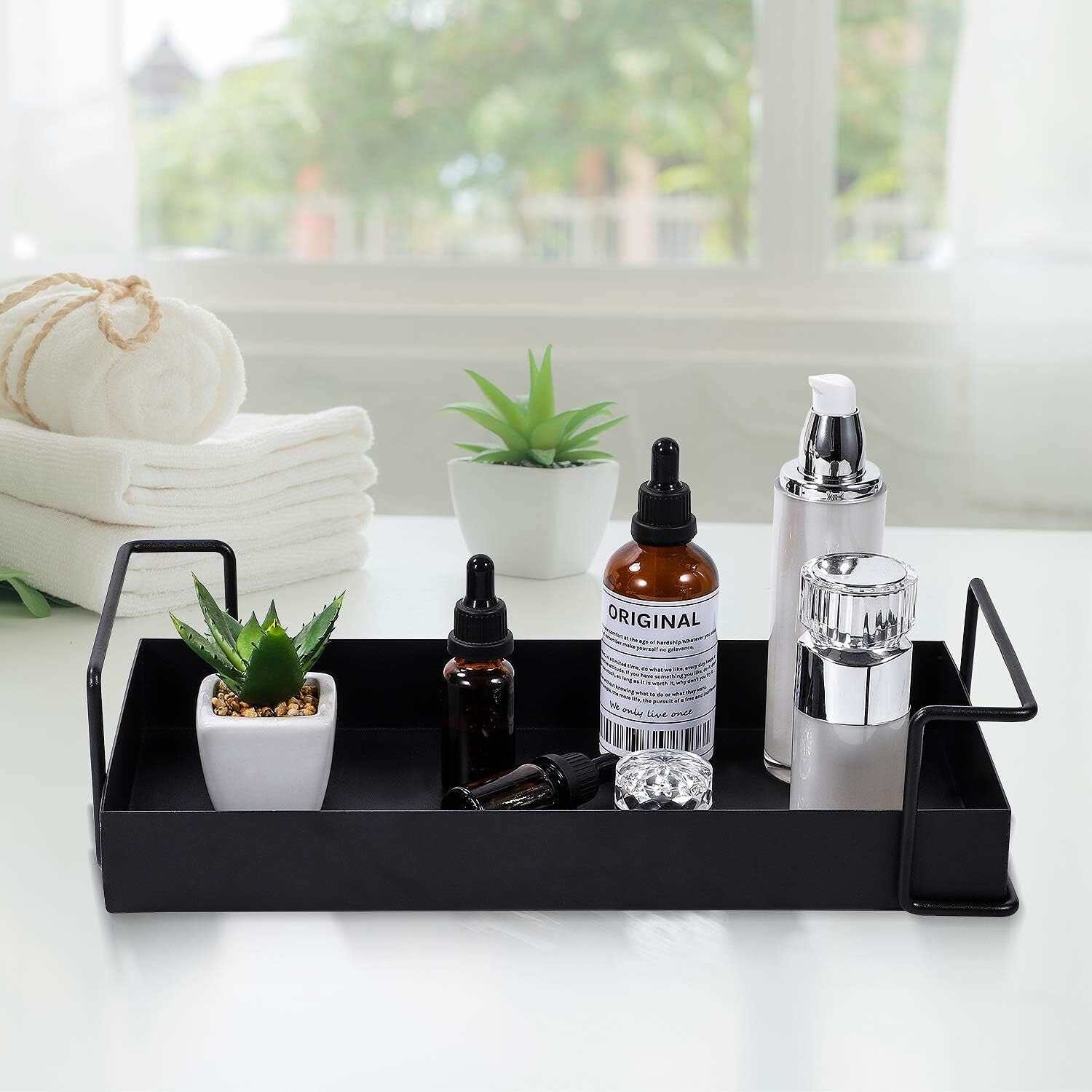 Black metal bathroom vanity tray with essential oils and decor items on a white countertop.